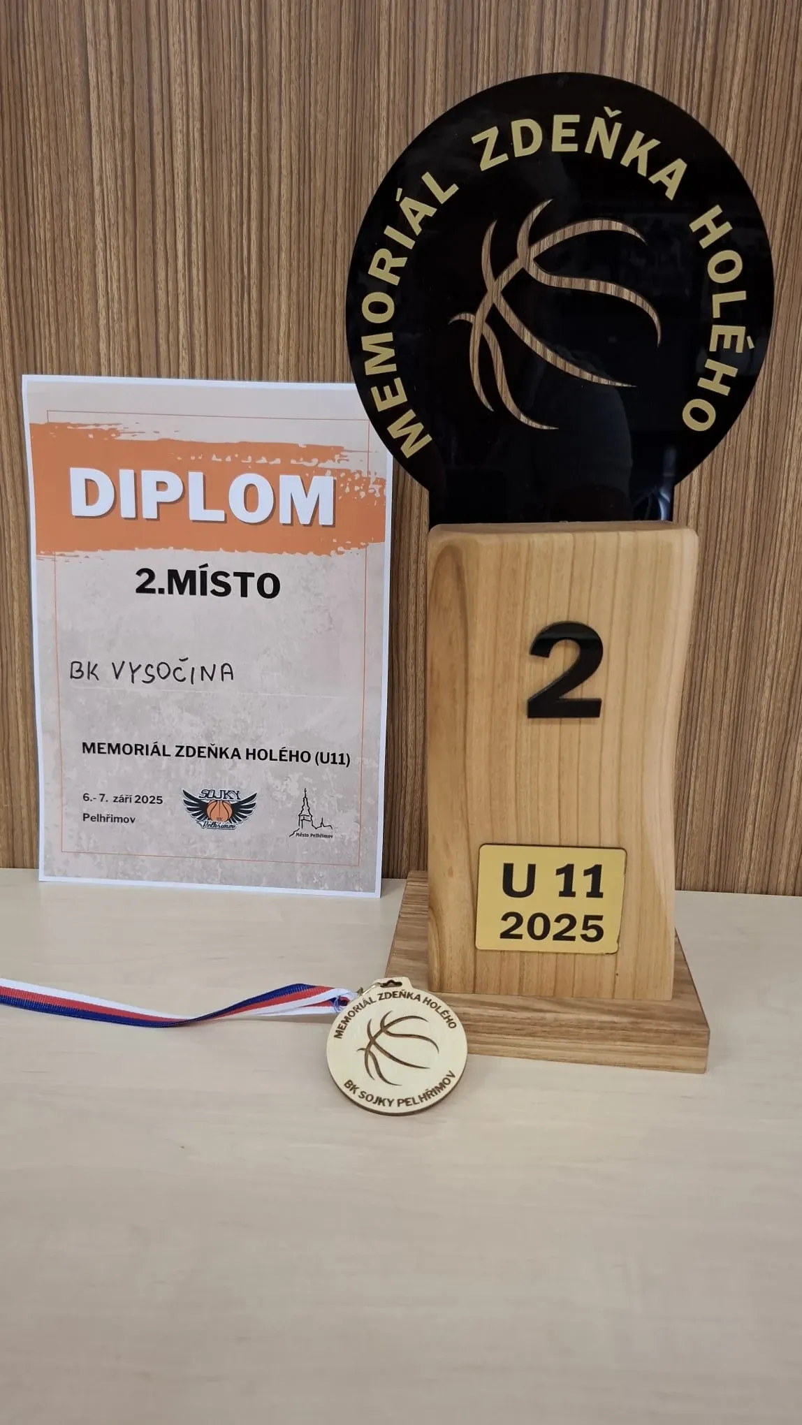 Diplom za 2. místo pro BK Vysočina z Memoriálu Zdeňka Holého (U11), 6.–7. září 2025 v Pelhřimově, vedle trofeje s číslem 2 a štítkem U11 2025 a dřevěné medaile BK Sojky Pelhřimov.